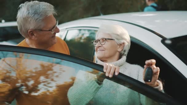 Το ηλικιωμένο ζευγάρι αγόρασε καινούριο αυτοκίνητο. Στέκεται κοντά στην πόρτα και γυναίκα κρατώντας τα κλειδιά — Αρχείο Βίντεο