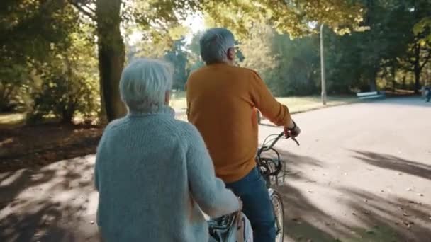 Starsza para jeżdżąca na podwójnym rowerze jesienią. Babcia i dziadek jadą razem na rowerze. Osoby w podeszłym wieku zdrowe i aktywne. — Wideo stockowe