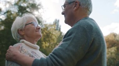 Sonbahar parkında dans eden mutlu yaşlı çift. Kıdemli adam yaşlı bir kadınla flört ediyor. Sonbahar günü parkta alnından öp.