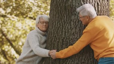 Ormanda romantik bir sonbahar günü geçiren yaşlı çift. Ağaca sarılmak ve gülümsemek