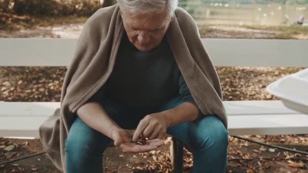 Pauvre homme âgé sans abri comptant les pièces laissées dans le parc et recevant un repas de charité — Video