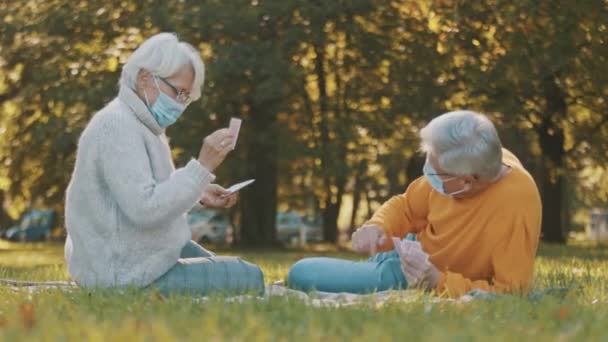Jubileumviering in het park tijdens covid-19. Ouderen paar met gezicht maskplaying kaartspel — Stockvideo