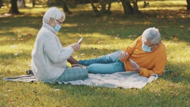 Anniversary celebration in the park during covid-19. Elderly couple with face maskplaying card game — Stock Video