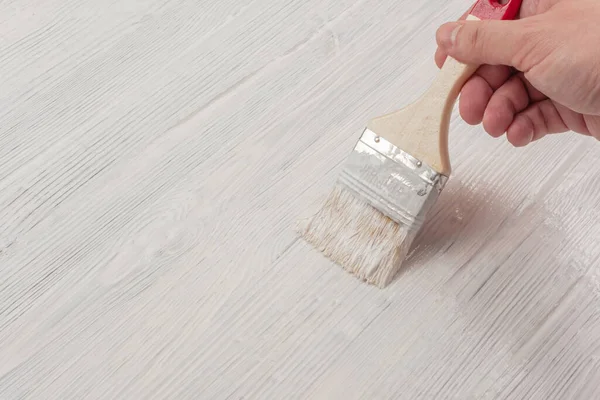 Fırçalanmış ahşap yüzey beyaz boyayla boyanmış ve erkek elinde fırça var.