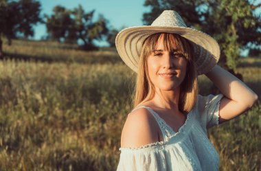 Yaz tatilinde gün batımında tarlada mutlu bir sarışın kadının yatay görüntüsü.