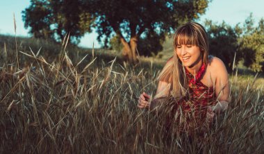 Gün batımında bir tarlada gülümseyen güzel sarışın manken elbise giyiyor. Doğada mutlu özgür bir kadın. Samimi fotoğrafçılık.