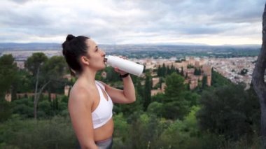 Egzersiz seansından sonra dinlenen ve su içen kadın Alhambra anıtının üzerinde tekrar kullanılabilir bir şişede. Spor salonundaki kadın egzersizden sonra mola veriyor..