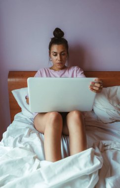 Genç bir kadın bilgisayarla video görüşmesi yaparken ve yatakta otururken telgraf çekiyor. Çevrimiçi sınıfta genç öğrenci.