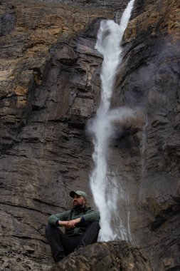 Takakkaw Şelalesinin önünde poz veren erkek yürüyüşçü