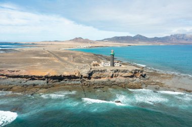 Uçsuz bucaksız deniz ufkuyla kayalık arazide duran, yukarıdan çekilen uzak deniz feneri..