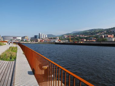 Brown iron railing next to the river with the city of Bilbao in the background