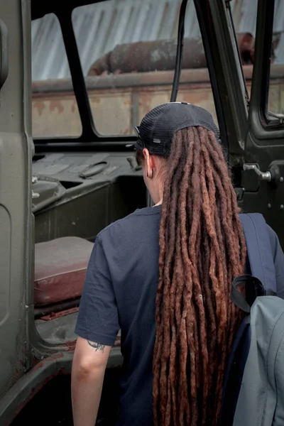 Rasta saçlı bir kız sırt çantasıyla ayakta duruyor. Kabinin arka planında.