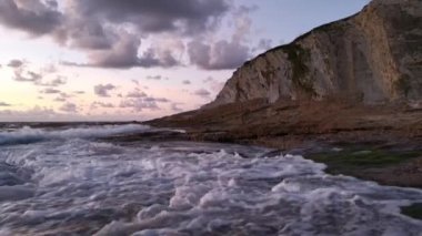 Sahilde bulutlu bir gün batımı. Dalgalar Alpenarri koyunda kayalara çarpıyor