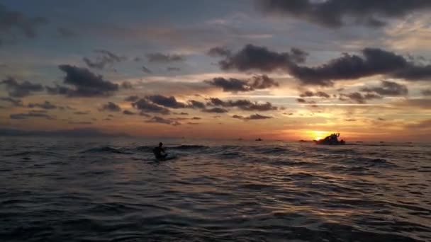 当太阳升起时 男孩在他的桨上划桨 背景中航行的船只的轮廓 — 图库视频影像