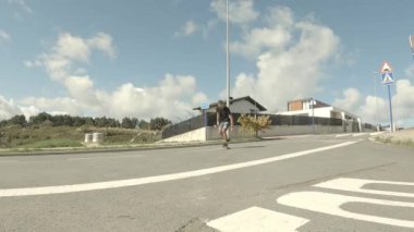 Siyah tişörtlü ve şortlu genç adam güneşli bir sabahta asfaltta kayıyor.
