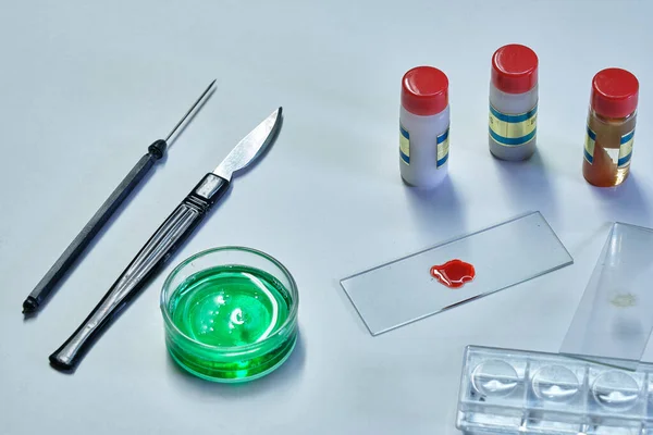 white laboratory table with scalpel glass bottle with green covid19 virus two small bottles with vaccine and blood sample, horizontal format