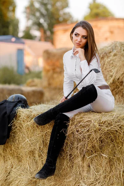 rider woman with whip is sitting on hay