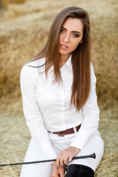 rider woman with whip is sitting on hay