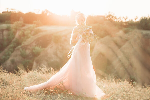 Portrait of the beautiful bride with bouquet of flowers against the sun in the nature. fine art photography.
