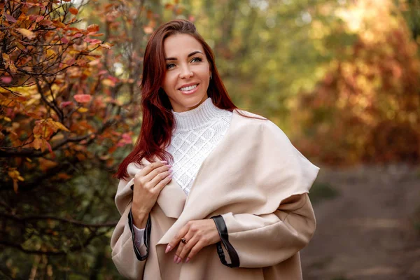 Vrouw in beige jas op een achtergrond van gele herfst bladeren — Stockfoto