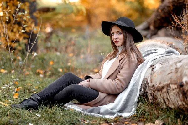 Belle femme en chapeau noir assis sous un grand arbre — Photo