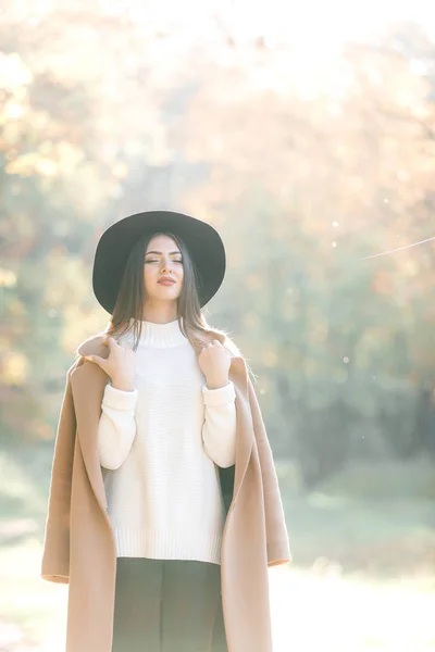 Hermosa joven con abrigo y sombrero negro en el parque — Foto de Stock