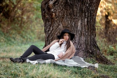 büyük ağacın altında oturan siyah şapkalı güzel kadın