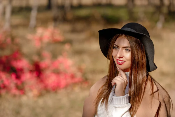 Mooie jonge vrouw in de jas en zwarte hoed — Stockfoto
