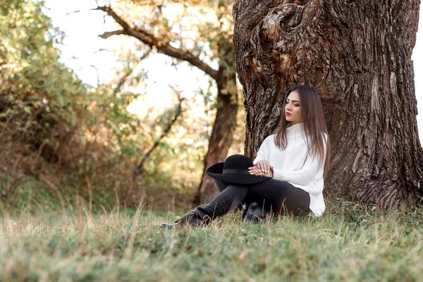 Büyük ağacın altında oturan siyah şapkalı güzel kadın — Stok fotoğraf