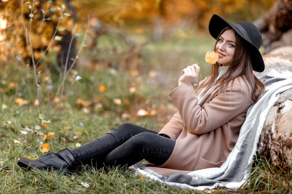 Schöne Frau mit schwarzem Hut sitzt unter großem Baum — Stockfoto