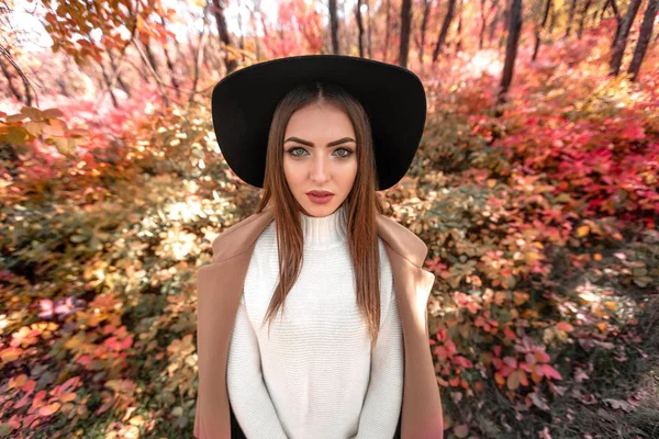 Vrouw in zwarte hoed op de achtergrond van de herfst bladeren. — Stockfoto