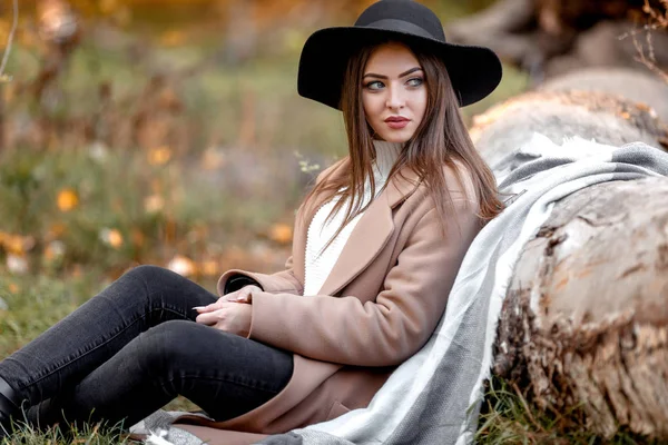 Mooie vrouw in zwarte hoed zitten onder een grote boom — Stockfoto