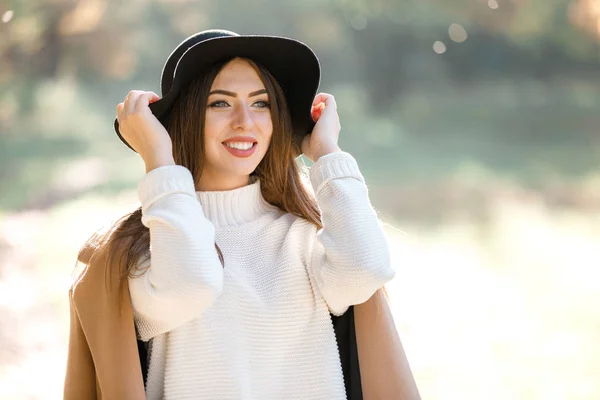 Bella giovane donna in cappotto e cappello nero nel parco — Foto Stock
