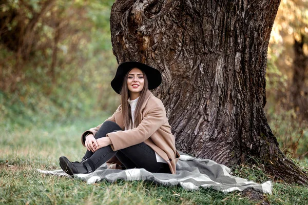 Beautiful woman in black hat sitting under big tree — Stock Photo, Image