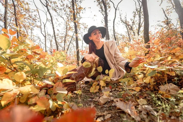 Женщина в платье и шляпе на фоне осенней листвы — стоковое фото