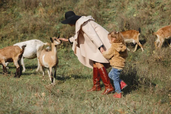 Moeder loopt met dochtertje in de buurt van een kudde geiten in de herfst — Stockfoto