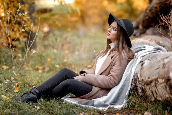 Schöne Frau mit schwarzem Hut sitzt unter großem Baum — Stockfoto