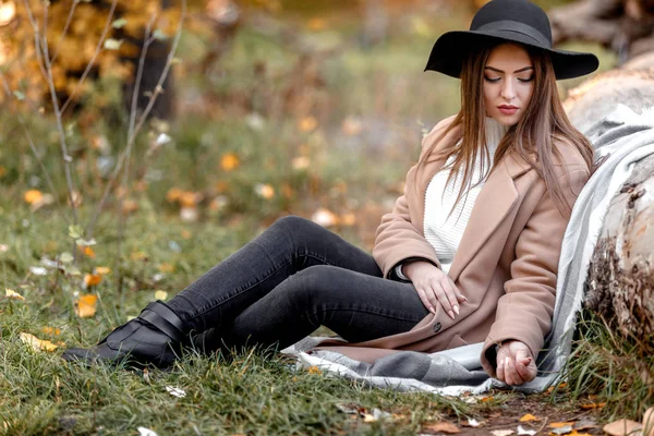 Schöne Frau mit schwarzem Hut sitzt unter großem Baum — Stockfoto