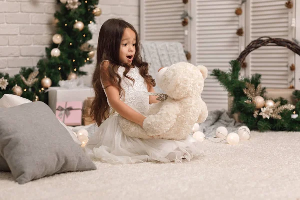 Дитяча дівчина грає з плюшевим ведмедем біля ялинки — стокове фото