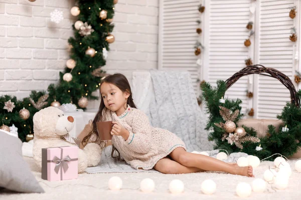 Мила дівчина п'є гаряче какао і грає з плюшевим ведмедем вдома. Різдво — стокове фото