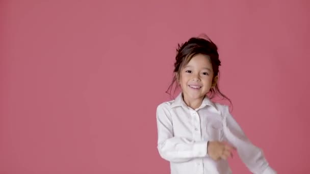 Niña pequeña en camisa blanca bailando sobre fondo rosa . — Vídeo de stock