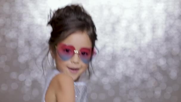 Lindo niño niña feliz en un vestido de plata bailando sobre fondo de plata bokeh . — Vídeo de stock