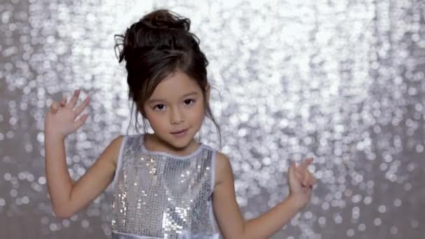 Roztomilý šťastné malé dívek v stříbrné šaty, tanec na pozadí stříbrné bokeh. — Stock video