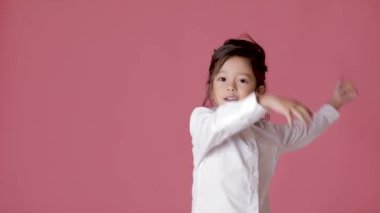küçük çocuk kız beyaz gömlekli, pembe arka plan dans.