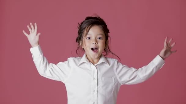 Мила маленька дівчинка в білій сорочці показує різні емоції на рожевому фоні . — стокове відео