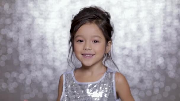 Mooie glimlachend kind meisje in een zilveren jurk dansen op achtergrond van zilveren bokeh. — Stockvideo