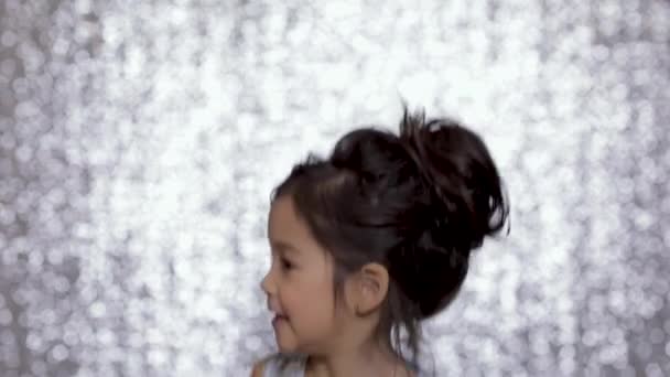 Bonito criança menina feliz em um vestido de prata dançando no fundo do bokeh de prata . — Vídeo de Stock