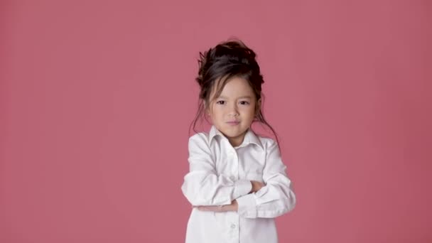 Милая маленькая девочка в белой рубашке показывает различные эмоции на розовом фоне . — стоковое видео