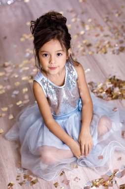 konfeti ile katta oturan mavi elbiseli küçük kız