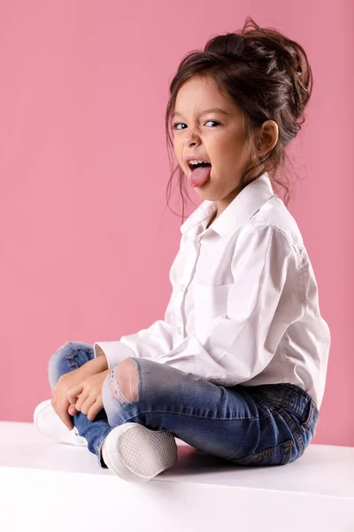 Мила маленька дівчинка в білій сорочці з зачіскою, що показує язик — стокове фото